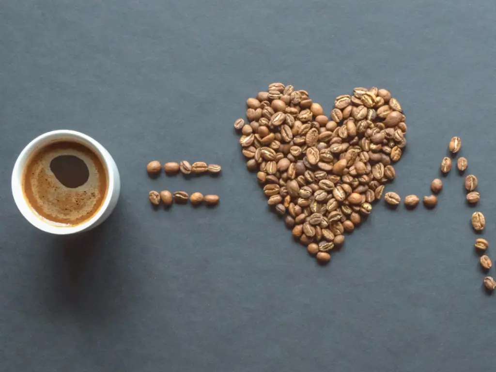 A cup of coffee with a heart cardiogram on a black table shows if is coffee good for your heart or not.